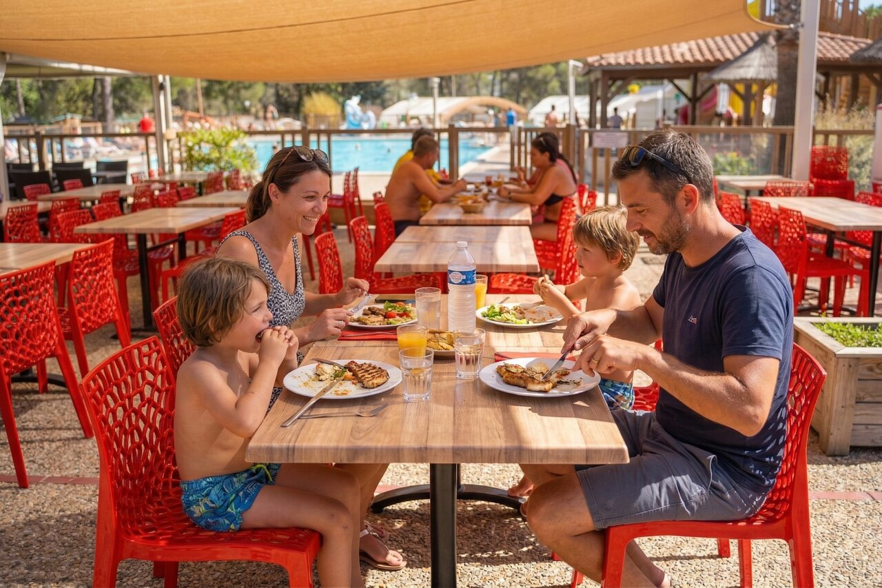 Familie luncht in buitenrestaurant bij zwembad op camping CAPFUN Arbois du Castellet in LE CASTELLET (83).