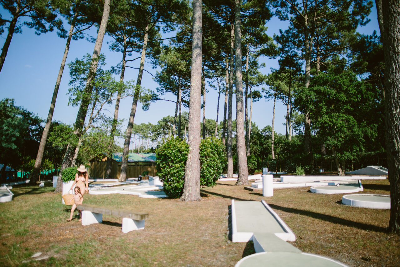 Schaduwrijke minigolfbaan onder pijnbomen met familie op camping LIBRANOO Naturiste Arnaoutchot in Veille-Saint-Girons, Landes, Frankrijk.