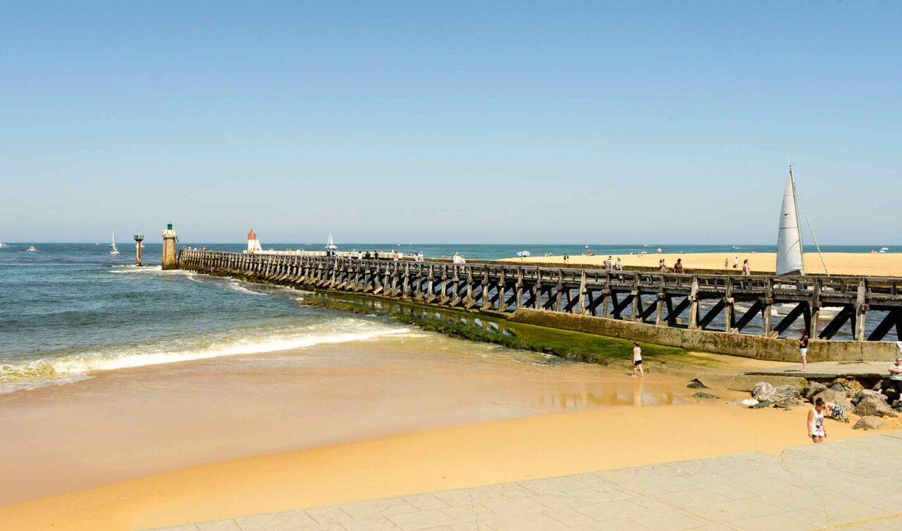 Zandstrand, houten pier, zeilboten op camping LIBRANOO Naturiste Arnaoutchot.