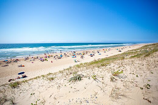 Breed zandstrand met zwemmers en parasols op camping LIBRANOO Naturiste Arnaoutchot in Veille-Saint-Girons, Landes, Frankrijk.