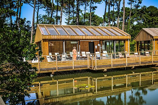 Houten spa gebouw met terras aan het water op camping LIBRANOO Naturiste Arnaoutchot in Veille-Saint-Girons, Landes, Frankrijk.