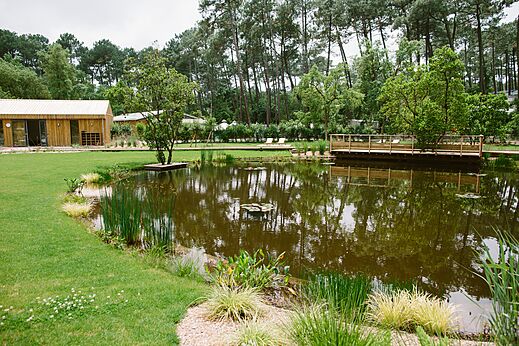 Natuurlijke vijver, groen en houten gebouwen op camping LIBRANOO Naturiste Arnaoutchot.