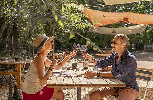Koppel proostend in het schaduwrijke buitenrestaurant van camping CLICOCHIC Art de Vivre in Ch�teauneuf du Pape.