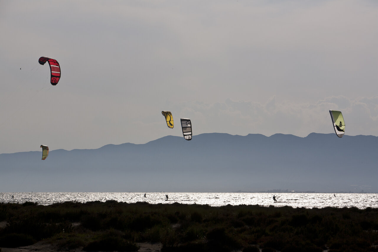 Kitesurfers op sprankelend water met bergen op camping CAPFUN Aube in Deltebre, Tarragona.