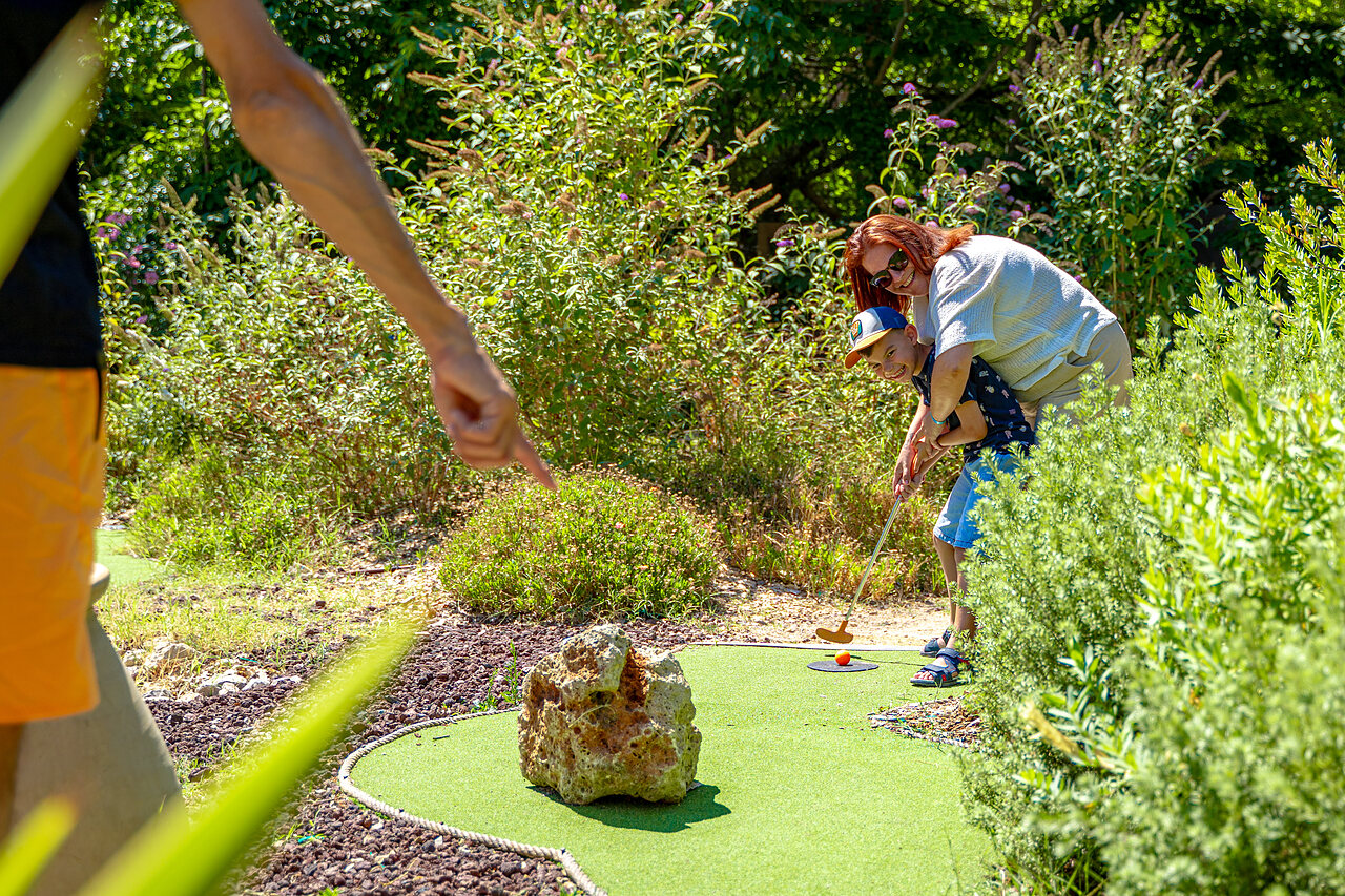 Kind en volwassene spelen minigolf op een groene baan op camping CAPFUN Aubr�des in Puget sur Argens (83).