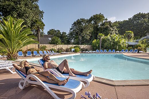 Buitenzwembad, stoelen en vakantiegangers op camping CLICOCHIC Baie de Douarnenez.