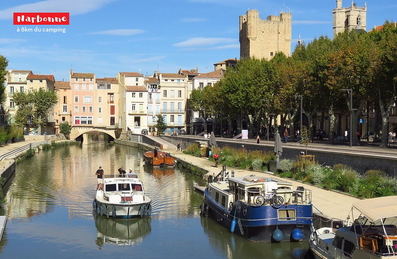 Canal de la Robine met boten, historische gebouwen en toren in Narbonne.