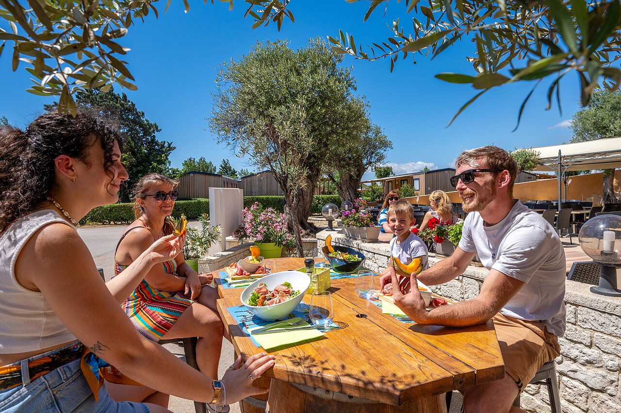 Lachende familie luncht op schaduwrijk terras, stacaravans op camping CAPFUN Barbacane in NARBONNE (11).
