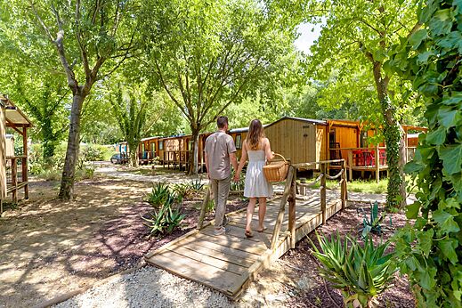 Paar wandelt naar schaduwrijke stacaravans op camping CAPFUN Bastide in Nîmes (30).