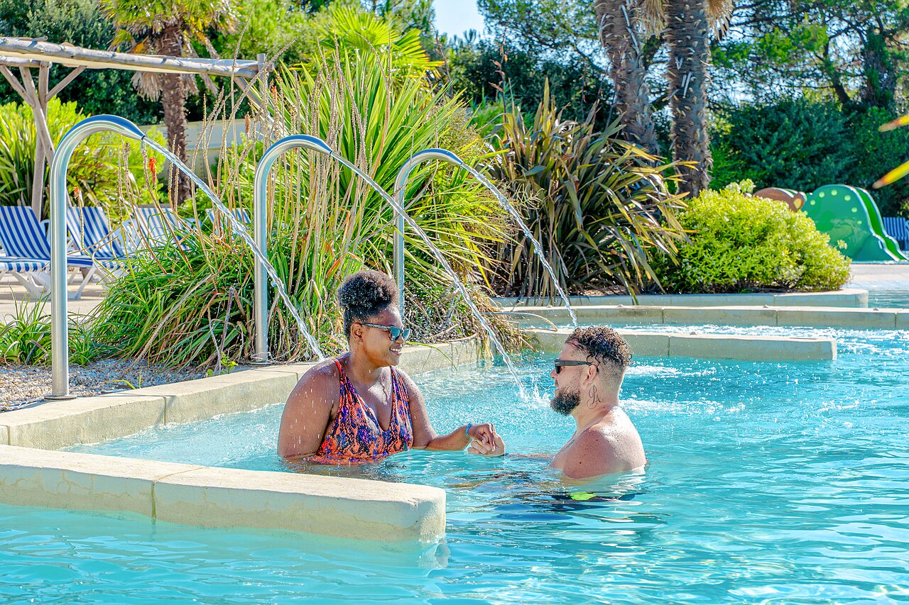 Koppel ontspant in het zwembad met waterstralen op camping VAGUES OCEANES Blancs Ch�nes in LA TRANCHE SUR MER (85).