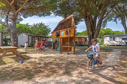 Speeltuin met houten structuur en kinderen op fiets op camping CAPFUN Bonne Etoile in BOIS PLAGE EN RE (17).