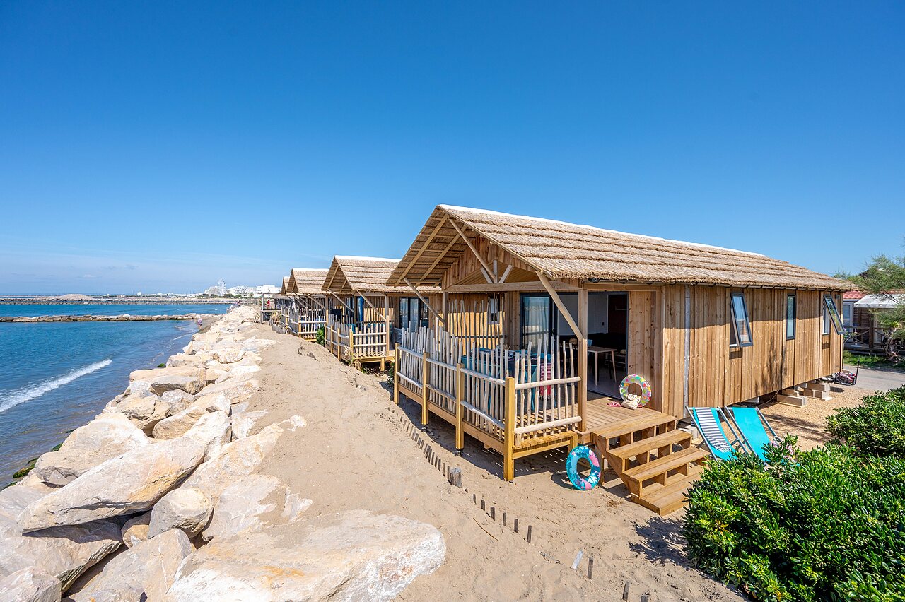 Houten chalets met rieten daken aan het strand op camping CAPFUN Boucanet in LE GRAU DU ROI (30).