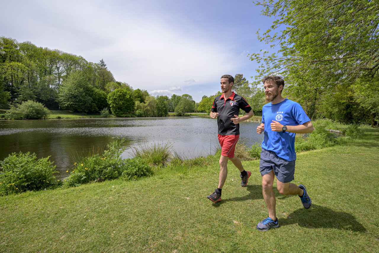 Twee mannen joggen langs een meer, groene natuurlijke omgeving, op camping CAPFUN Breteche in Les Epesses (85).