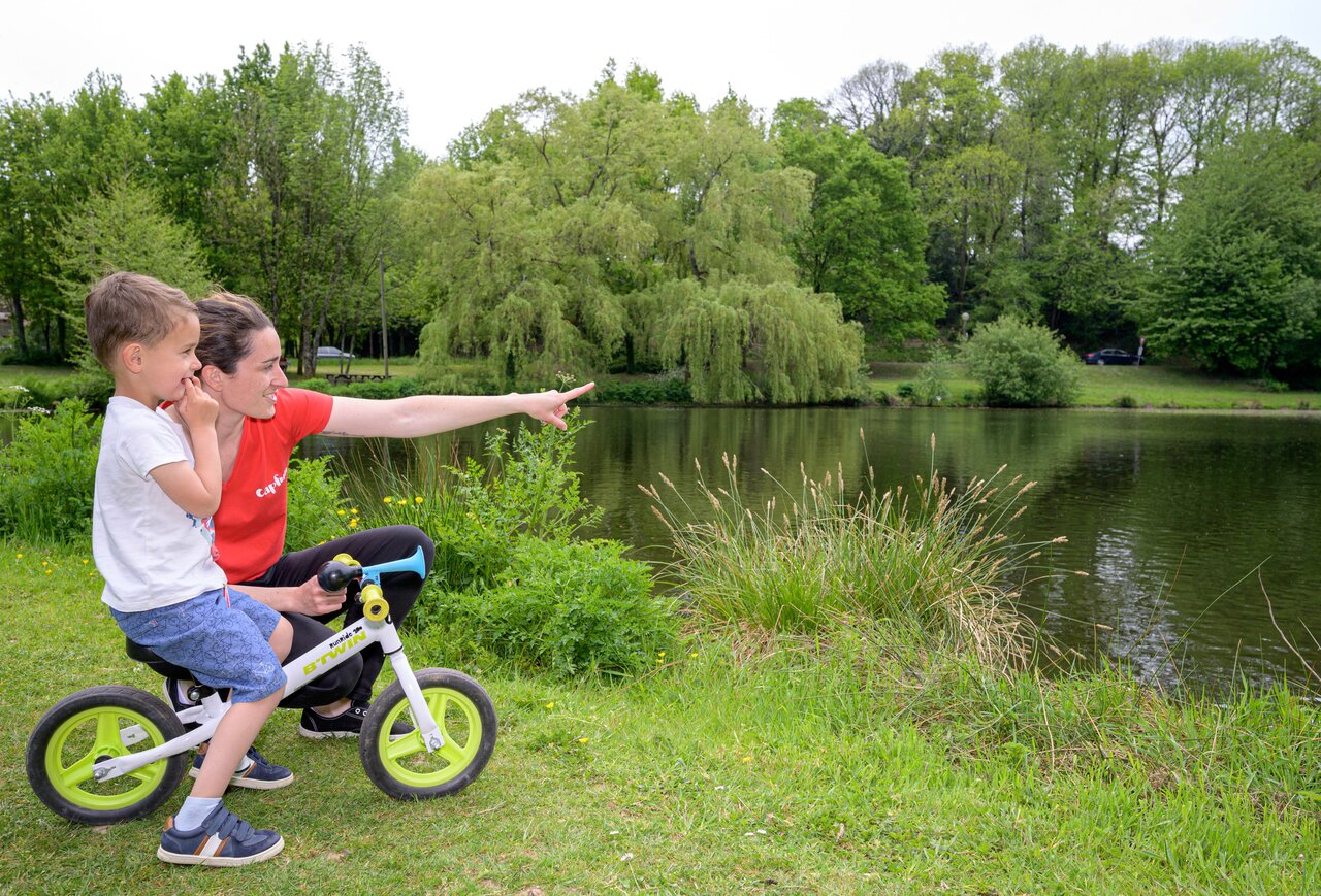 Kind op loopfiets en vrouw wijzend naar meer, natuur op camping CAPFUN Breteche in Les Epesses (85).