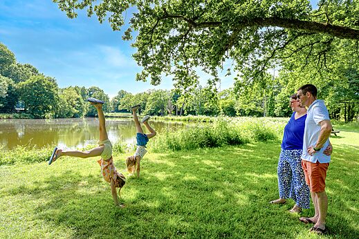 Kinderen doen handstanden bij meer, volwassenen kijken op camping CAPFUN Breteche (85).