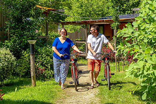 Paar wandelt met rode fietsen op groen pad bij camping CAPFUN Breteche in Les Epesses (85).