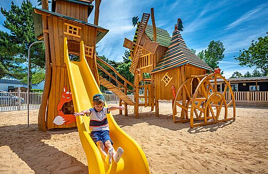 Kind op glijbaan, houten speeltuin op camping CLICOCHIC Cabanes d Oléron in ST GEORGES D'OLERON (17).