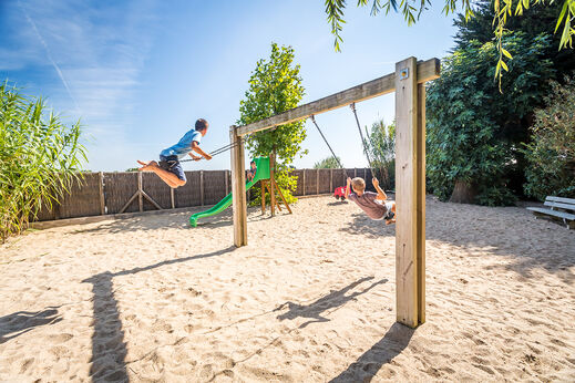 Twee kinderen spelen op schommels in de speeltuin op camping CLICOCHIC Camp du Soleil in Ars-en-Ré (17).