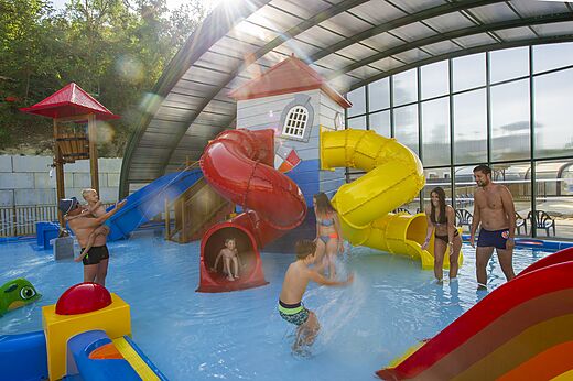 Waterglijbanen en waterspellen in het overdekte zwembad van camping CAPFUN Carpe Diem.