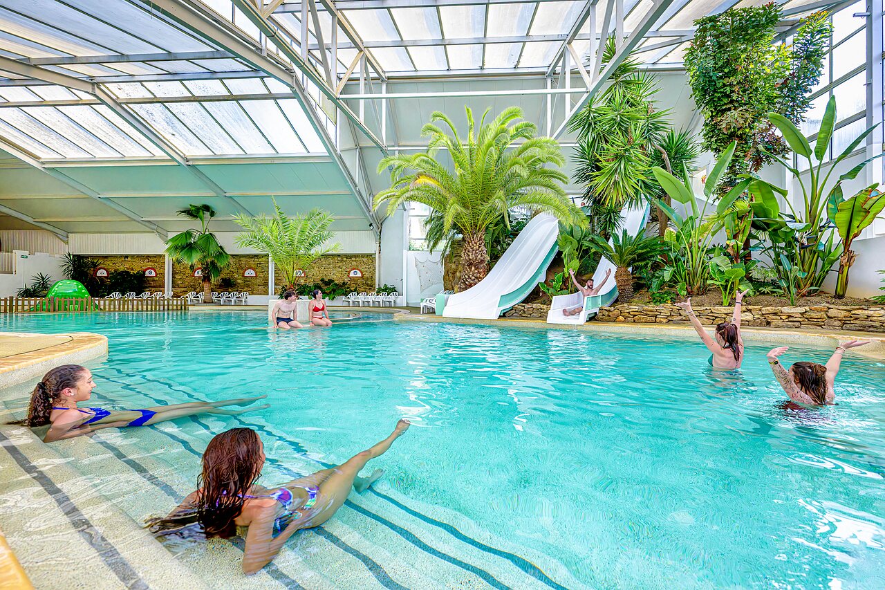 Overdekt zwembad met glijbanen en palmbomen op camping CAPFUN Cenic in PENESTIN (56).