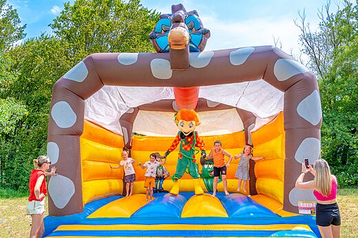 Groot opblaasbaar springkasteel met kinderen en mascotte op camping CLICOCHIC Chancia in Chancia (01).