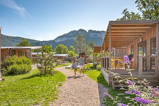 Houten stacaravans met terrassen en wandelend stel op camping CLICOCHIC Chancia in Chancia (01).