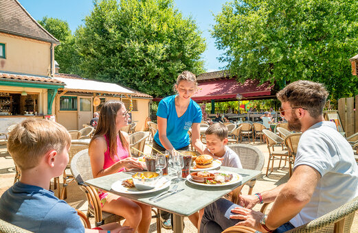 Familie luncht op het restaurantterras op camping VAGUES OCEANES Chataigneraie in Prats-de-Carlux.