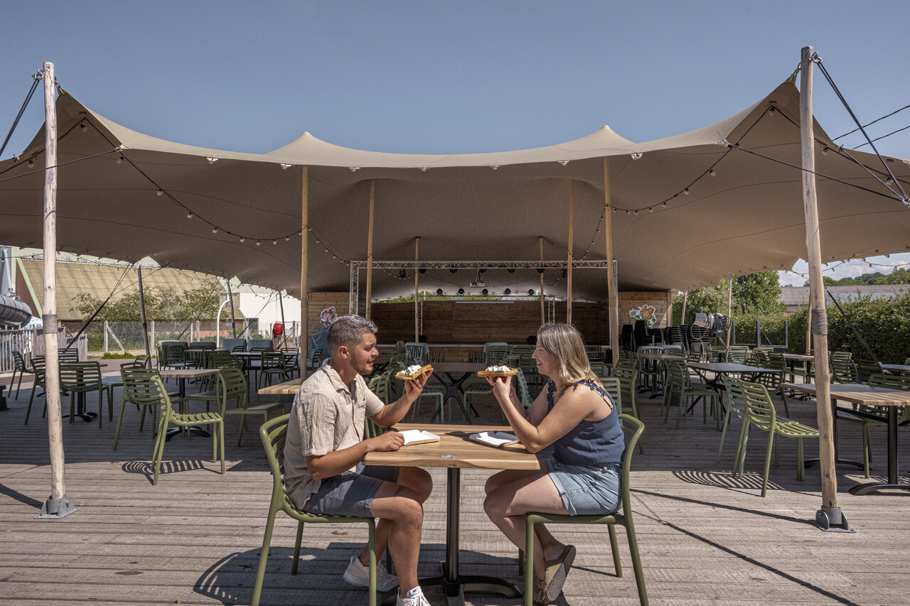 Koppel eet op geanimeerd restaurantterras op camping CLICOCHIC Chevaliers in HOULGATE.