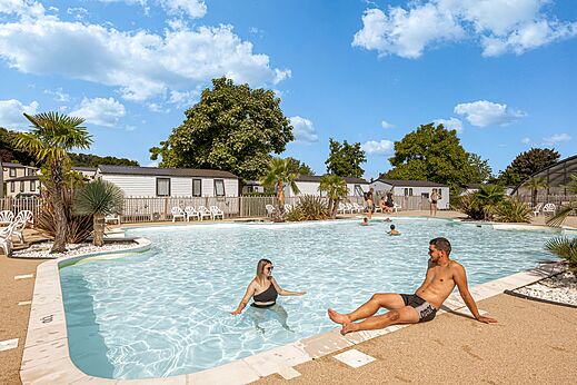 Buitenzwembad met zwemmers en stacaravans op camping CLICOCHIC Chevaliers in HOULGATE (14).