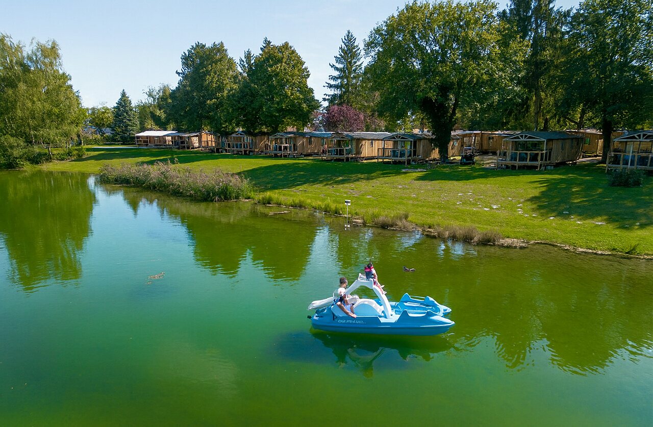 Waterfiets op het meer met houten accommodaties op camping CLICOCHIC Au Clair Ruisseau in Gerstheim (67).