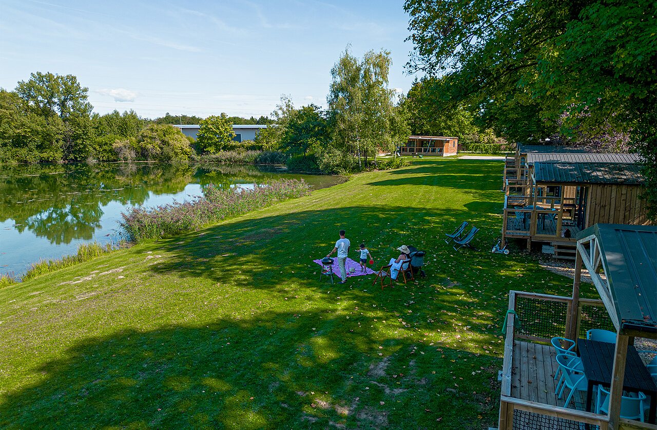 Houten hutten, meer en gezin picknickend op camping CLICOCHIC Au Clair Ruisseau.
