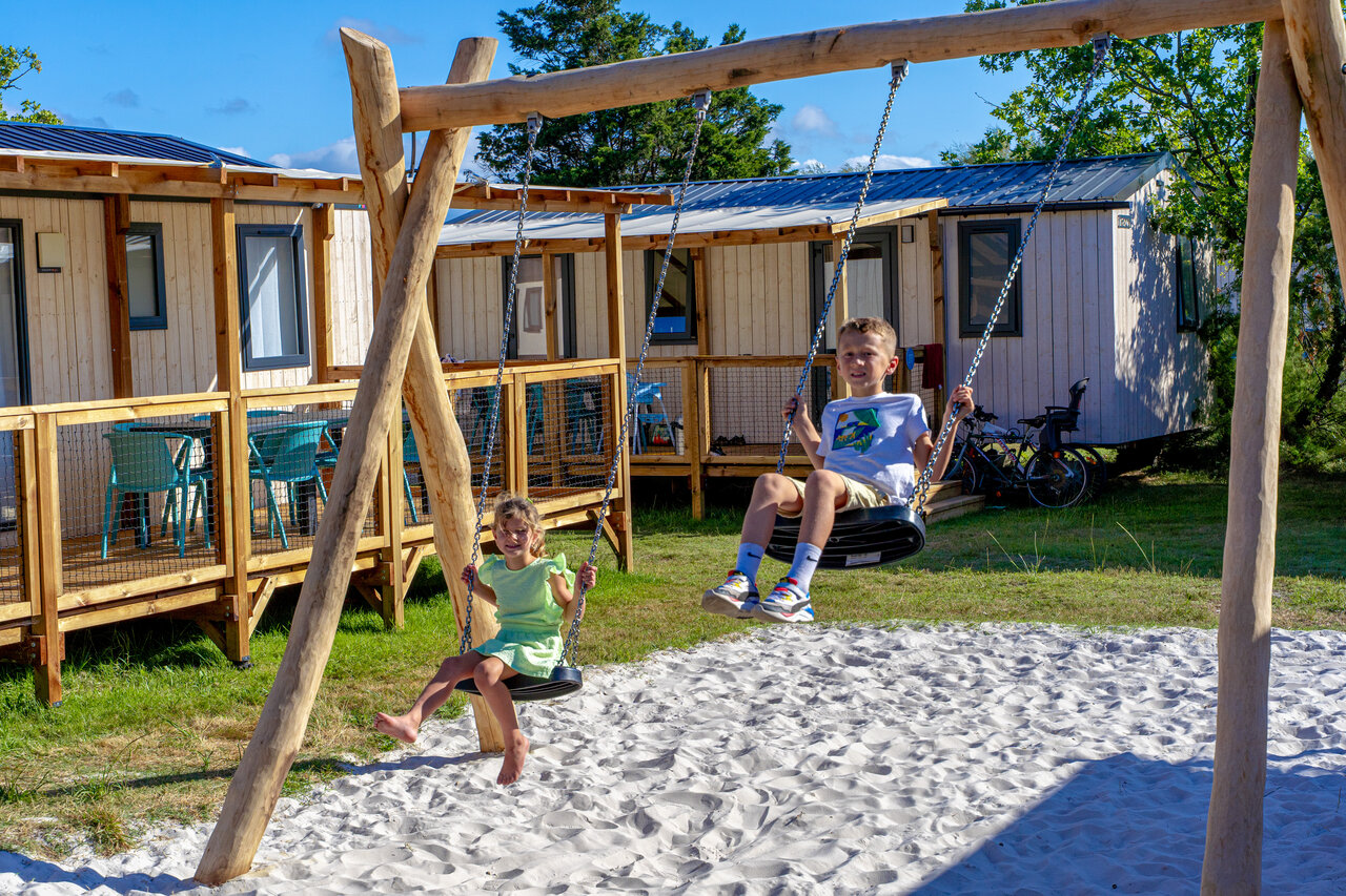 Kinderen spelen op houten schommel voor stacaravans op camping VAGUES OCEANES Coq Hardi in Cassy-Lanton (33).