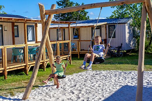 Kinderen spelen op de schommels, stacaravans op camping VAGUES OCEANES Coq Hardi.