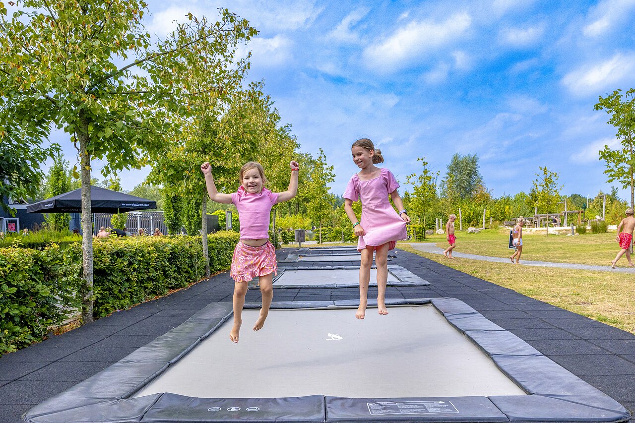 Vrolijke kinderen springen op ingegraven trampolines op camping CAPFUN De Belten in Rheeze.