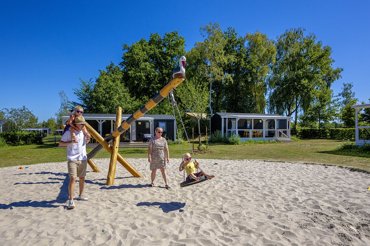 Zand speeltuin met schommel en familie, stacaravans op camping CAPFUN De Belten in Rheeze.
