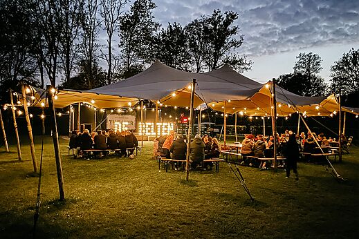 Buitenvoorstelling onder verlichte tent met publiek op camping CAPFUN De Belten in Rheeze.