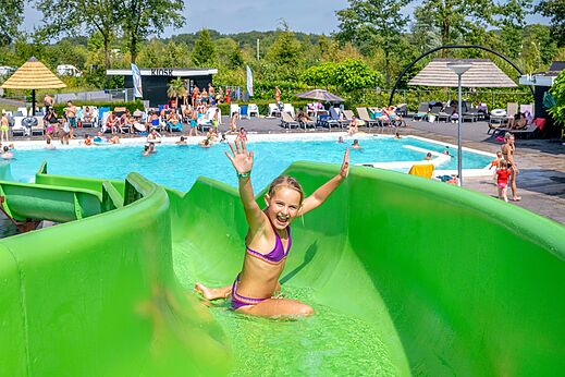 Lachend meisje op groene waterglijbaan en zwembad op camping CAPFUN De Belten in Rheeze.