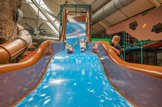 Grote binnenglijbaan met lachende kinderen op camping CAPFUN De Bongerd in Tuitjenhorn.