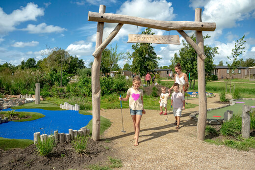 Familie speelt avonturengolf onder houten boog op camping CAPFUN De Bongerd in Tuitjenhorn.