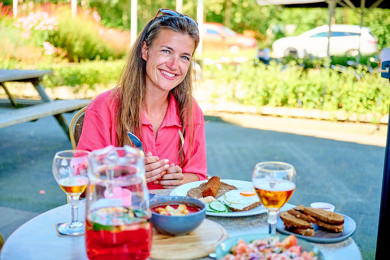 Lachende vrouw luncht op terras bij camping CAPFUN De Eikenhof in Paasloo/Oldemarkt.