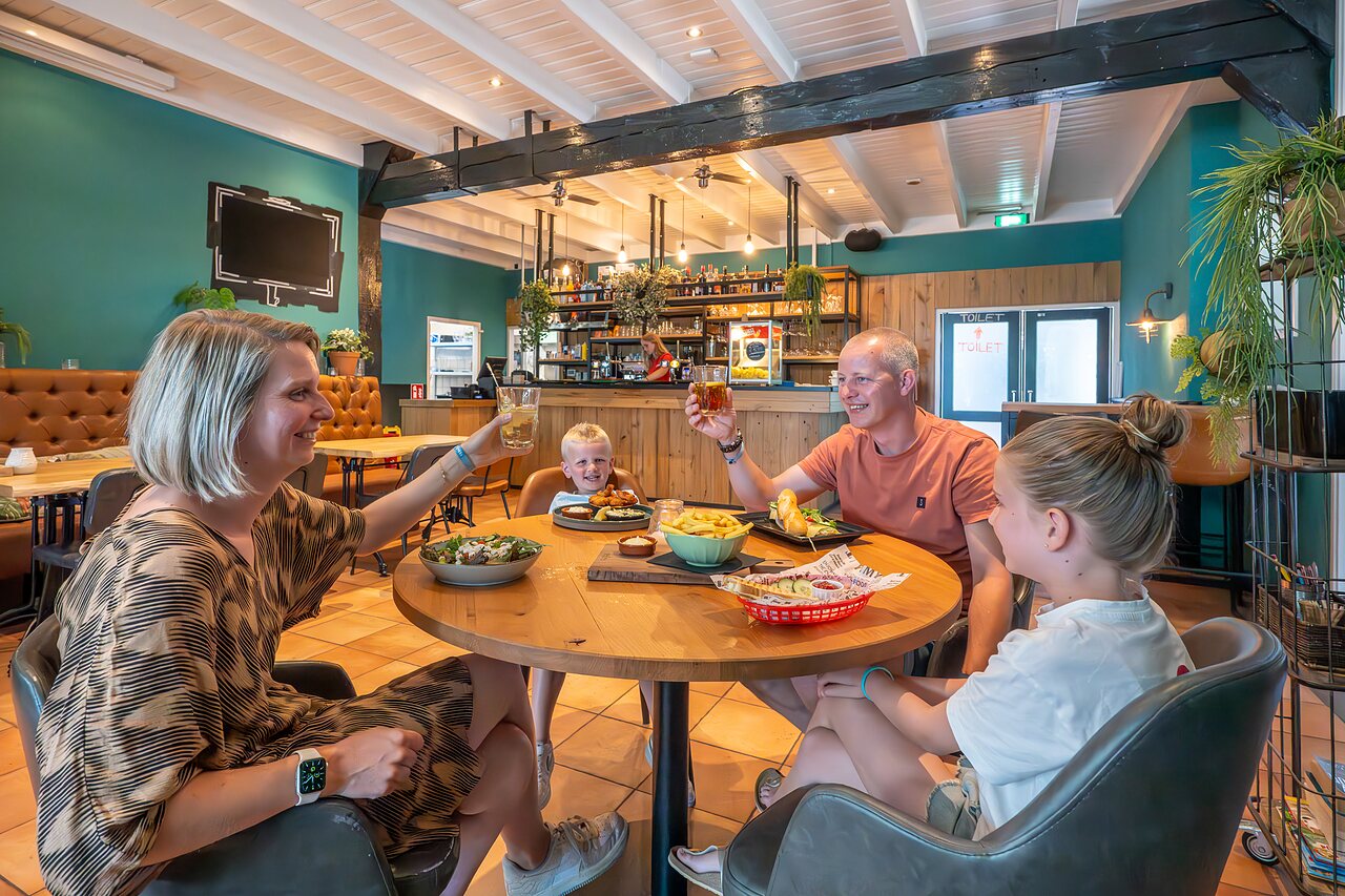 Lachende familie luncht in het restaurant van camping CAPFUN De Pekelinge in Oostkapelle.