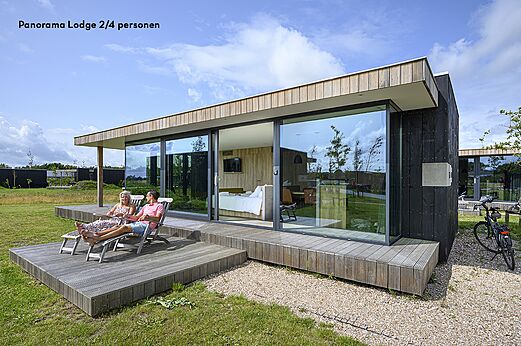 Moderne lodge met terras en ontspannend stel op camping CAPFUN De Pekelinge in Oostkapelle.