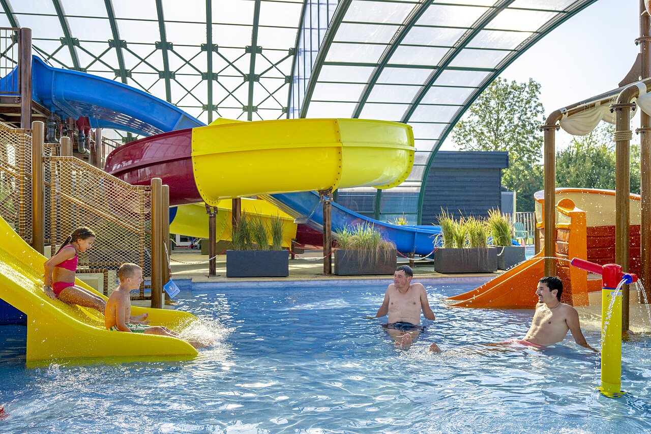 Kleurrijke waterglijbanen en overdekt zwembad met kinderen en volwassenen op camping CAPFUN De Rotonde in Enspijk.