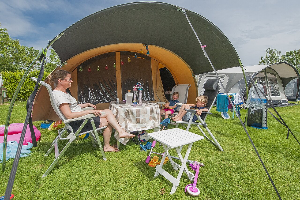 Familie ontspant op kampeerplaats met tent en luifel op camping CAPFUN De Rotonde in Enspijk.