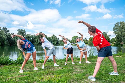 Jongeren doen rek- en strekoefeningen met animator op camping CAPFUN De Rotonde te Enspijk.