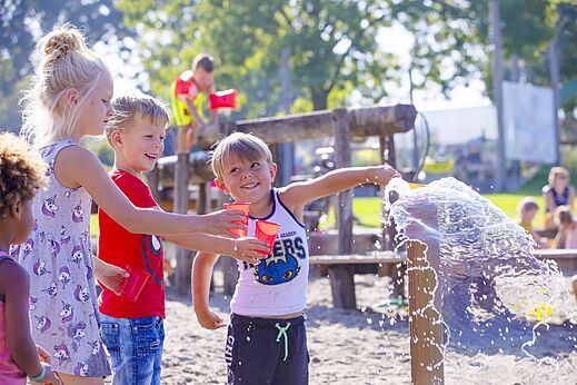 Vrolijke kinderen spelen met water en bekers op de speeltuin van camping CAPFUN De Rotonde in Enspijk.