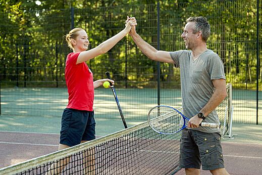 Tennisbaan met lachende spelers op camping CAPFUN De Scheepsbel in Doornspijk.