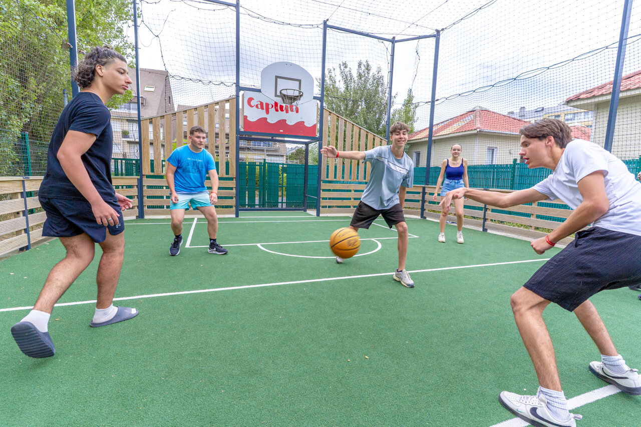 Jongeren basketballen op het multisportterrein van camping CAPFUN Donjon de Lars in Courseulles-sur-Mer.