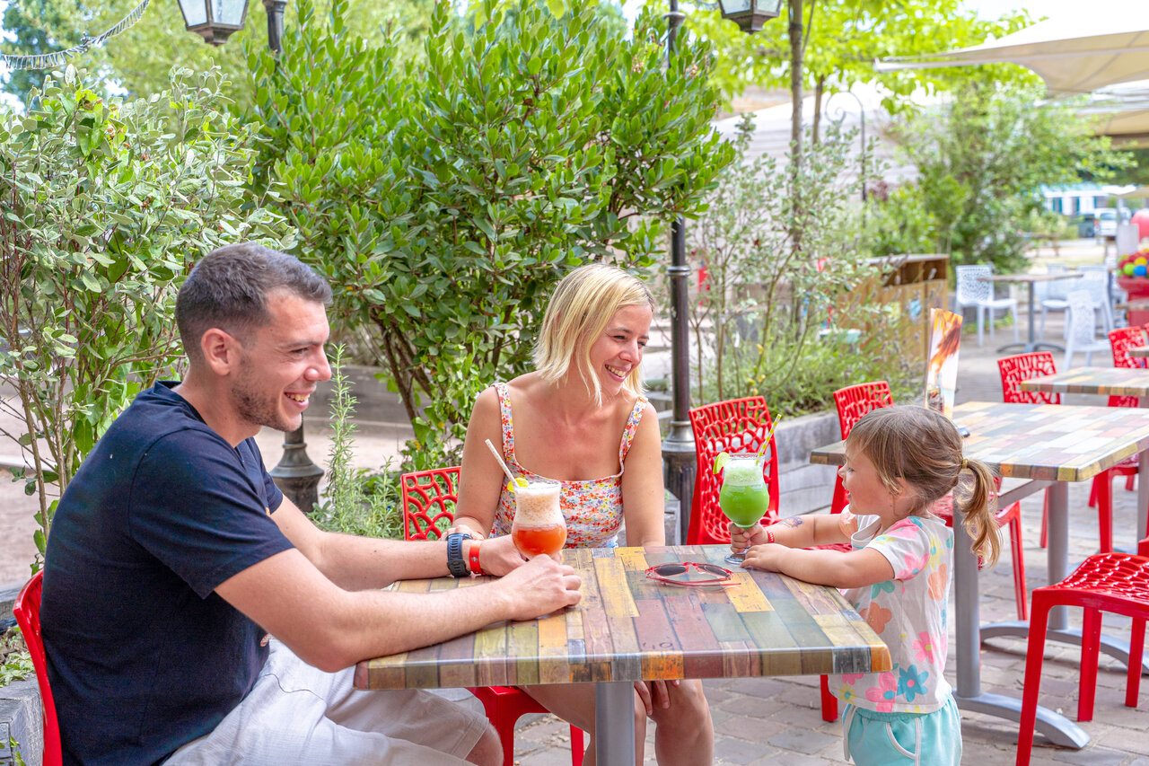 Lachende familie genietend van drankjes op terras restaurant, camping CAPFUN Donjon de Lars.