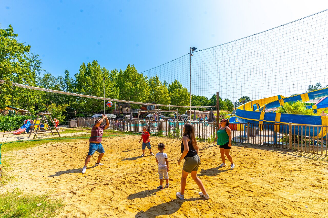 Familie speelt beachvolleybal op zandveld, waterglijbanen bij camping CAPFUN Duravel.